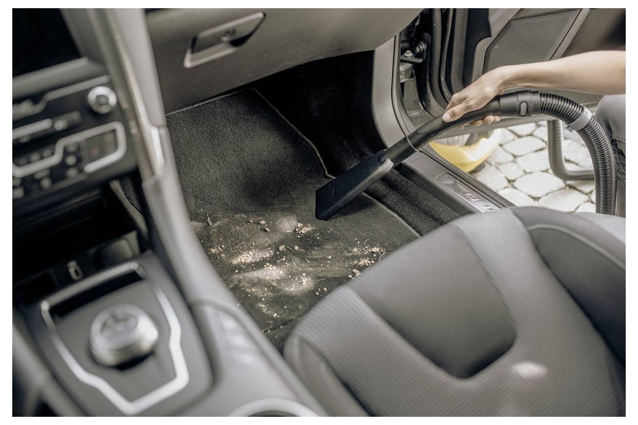 Eine Person, die den Boden des Autoinnenraums mit einem Staubsauger reinigt und Schmutz aus dem Teppich entfernt.