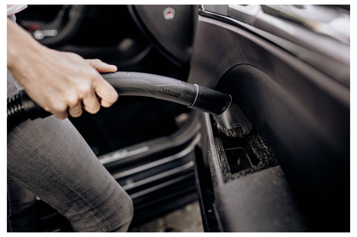 Eine Person, die das Innere eines Autos mit einem tragbaren Staubsauger reinigt und sich dabei auf den Spalt zwischen Sitz und Armaturenbrett konzentriert.