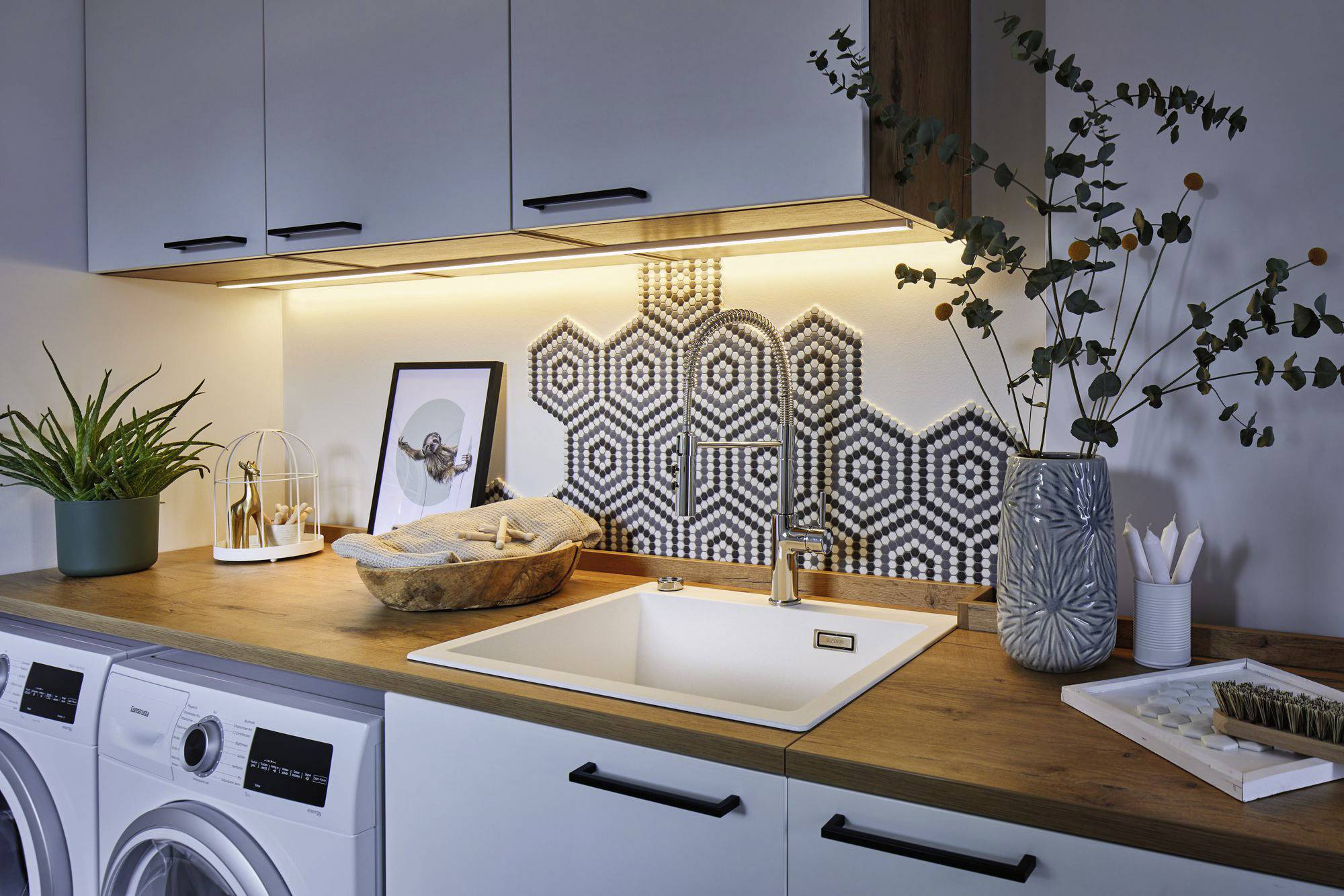 Waschküche mit Waschmaschine und Trockner, einem Holzarbeitsbereich mit Waschbecken und stilvollem Design, dekoriert mit Pflanzen.