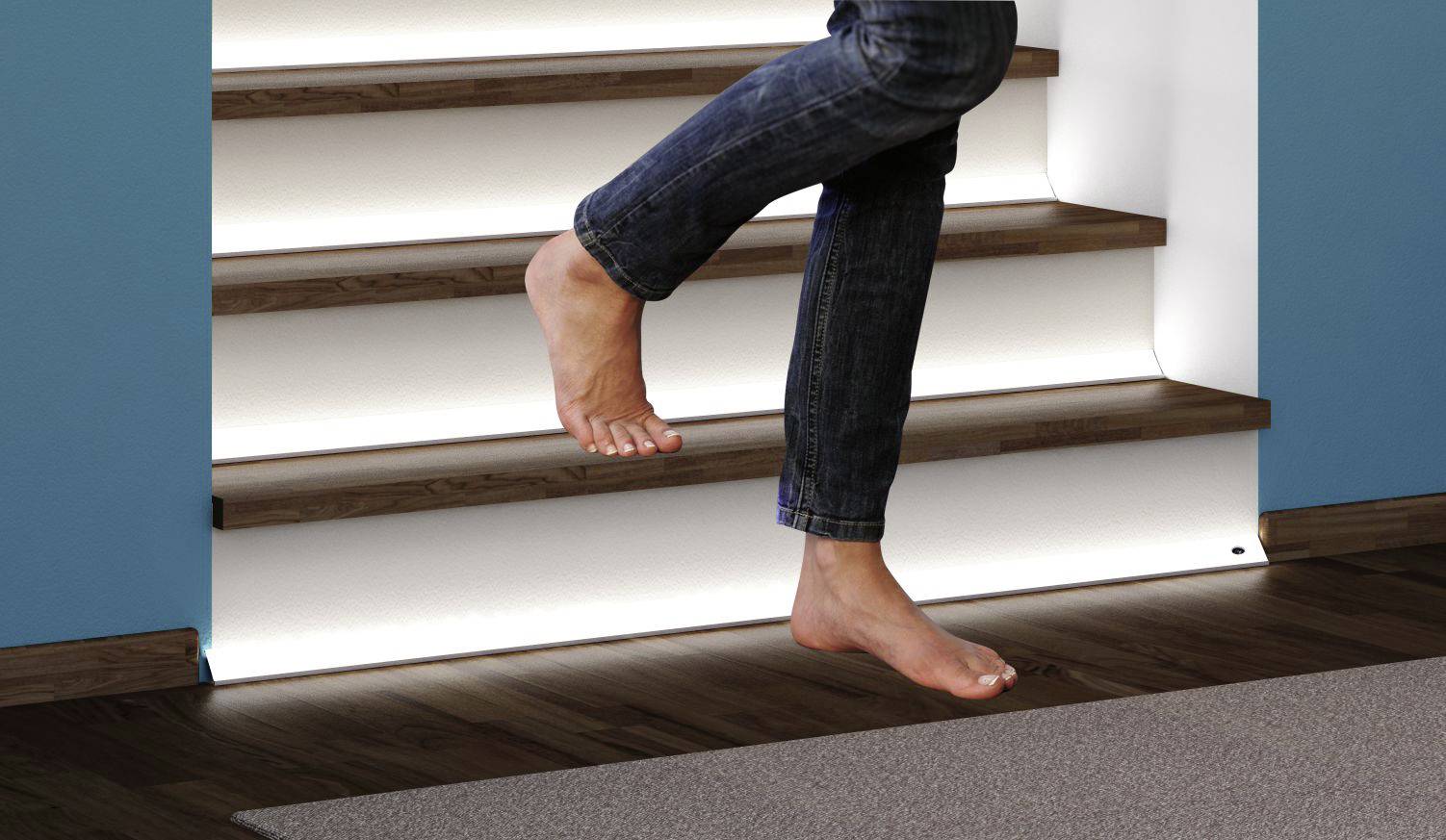 Person steigt barfuß eine Treppe im modernen Innenbereich hinauf. Treppenstufen sind mit indirekter Beleuchtung versehen.