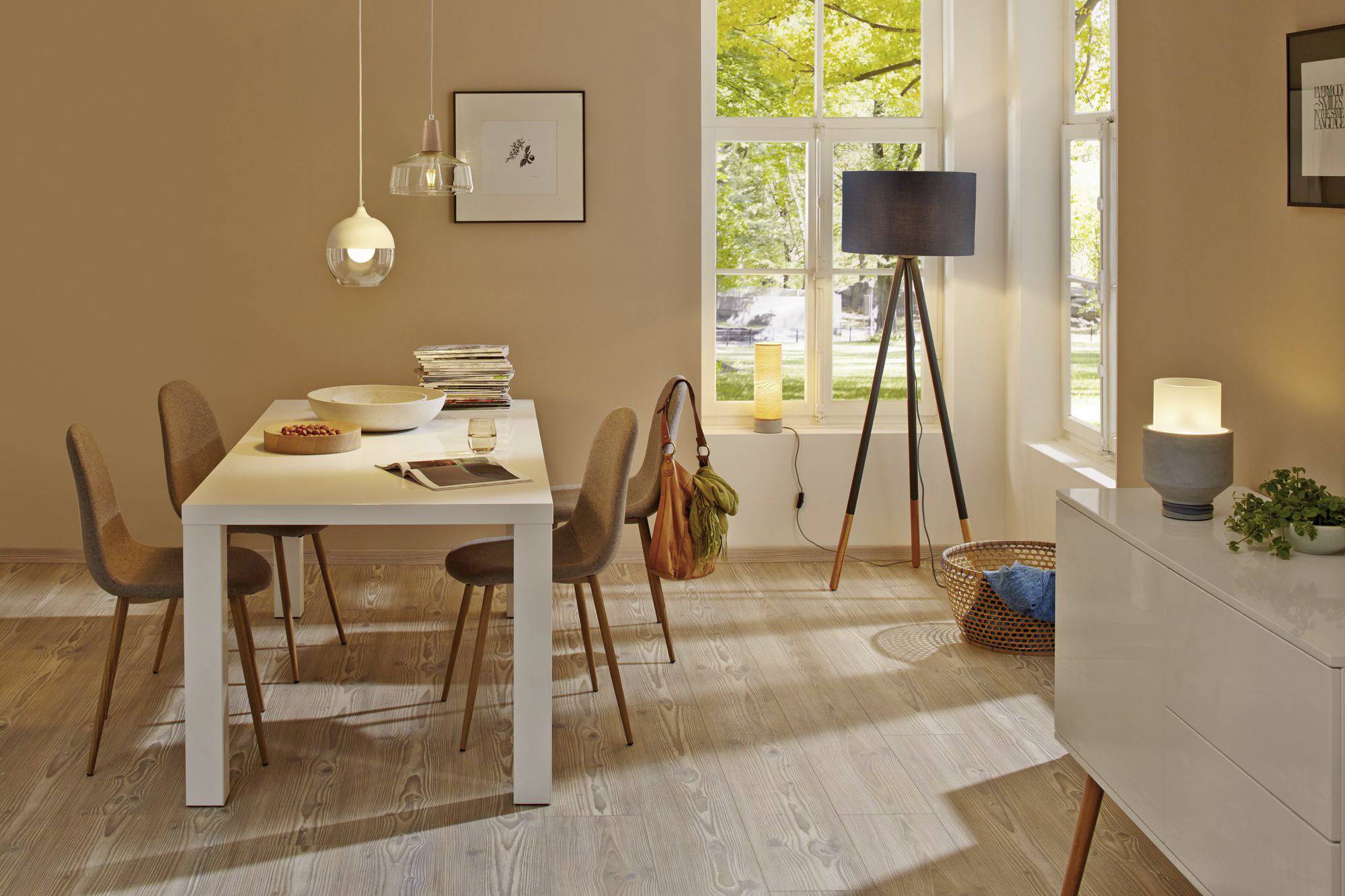 Gemütliches Wohnzimmer mit einem weißen Tisch und sechs Stühlen, sanft beleuchtet durch Pendelleuchten und Tageslicht von großen Fenstern.