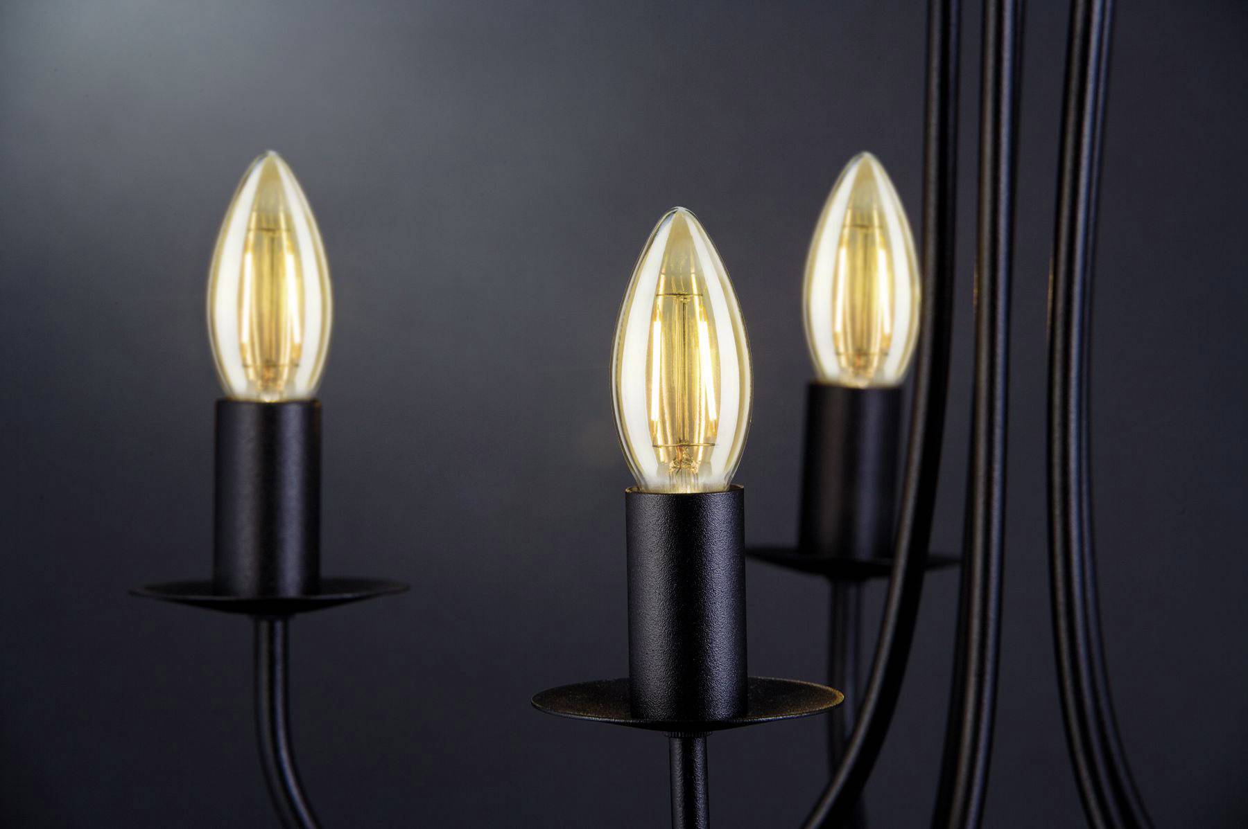 Drei Kerzenlampen in schwarzer Halterung leuchten warm auf dunklem Hintergrund. Modernes, minimalistisches Design.
