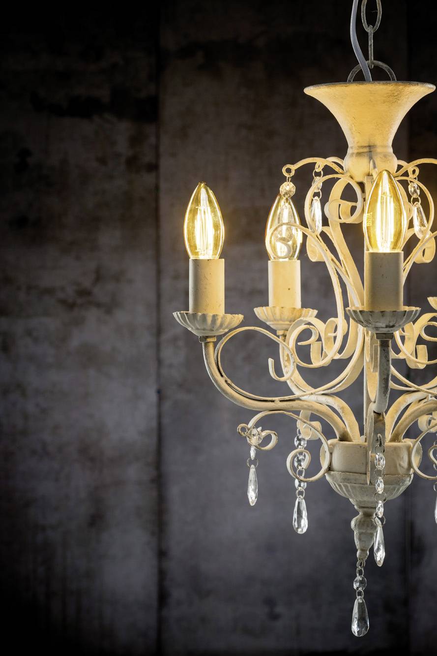 Ein dekorativer Kronleuchter mit drei leuchtenden Kerzenlampen und glitzernden Kristalltropfen hängt vor einem dunklen Hintergrund.