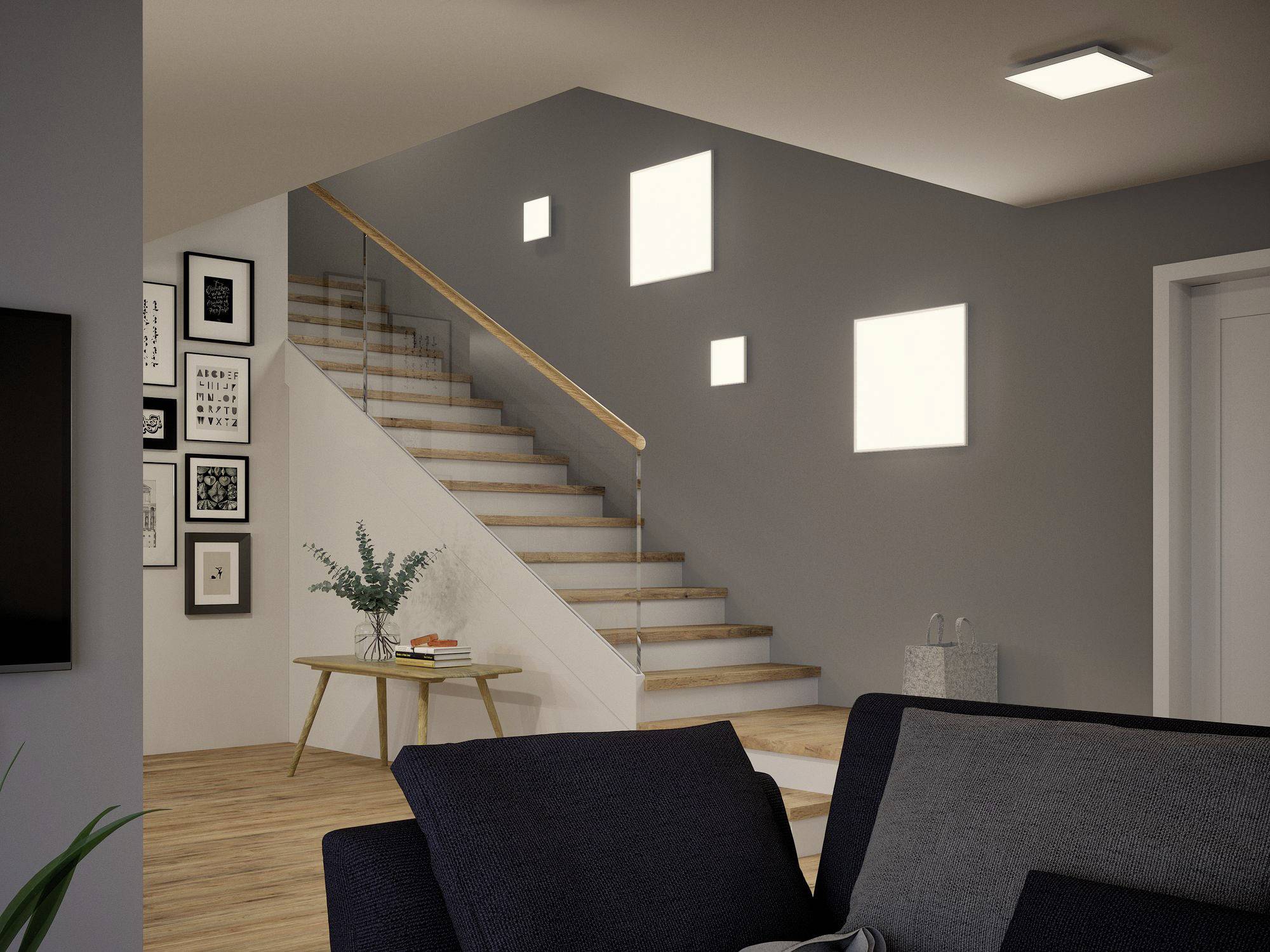 Treppenhaus in modernem Wohnraum mit Holzboden; weiße Treppe, graue Wand mit Bildern, Pflanzen auf Tisch und Beleuchtung an.