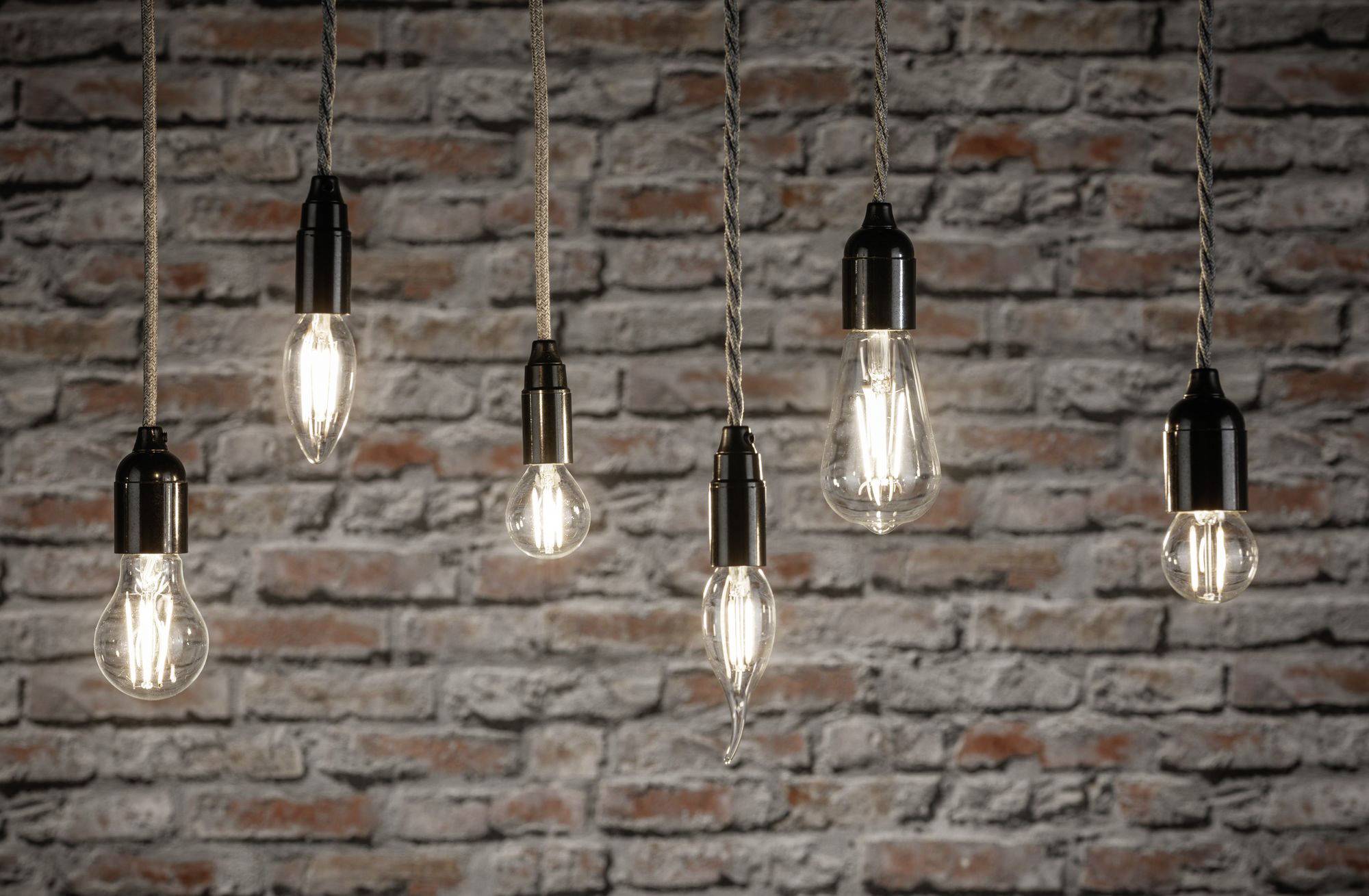 Sechs hängende Glühbirnen vor einer Ziegelwand leuchten schwach und schaffen eine rustikale, gemütliche Atmosphäre.