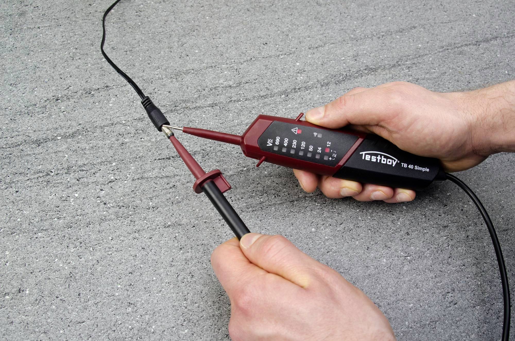 Eine Person testet ein Kabel mit einem elektronischen Prüfgerät auf einer grauen Oberfläche. Fokus liegt auf den Prüfspitzen und dem Gerät.