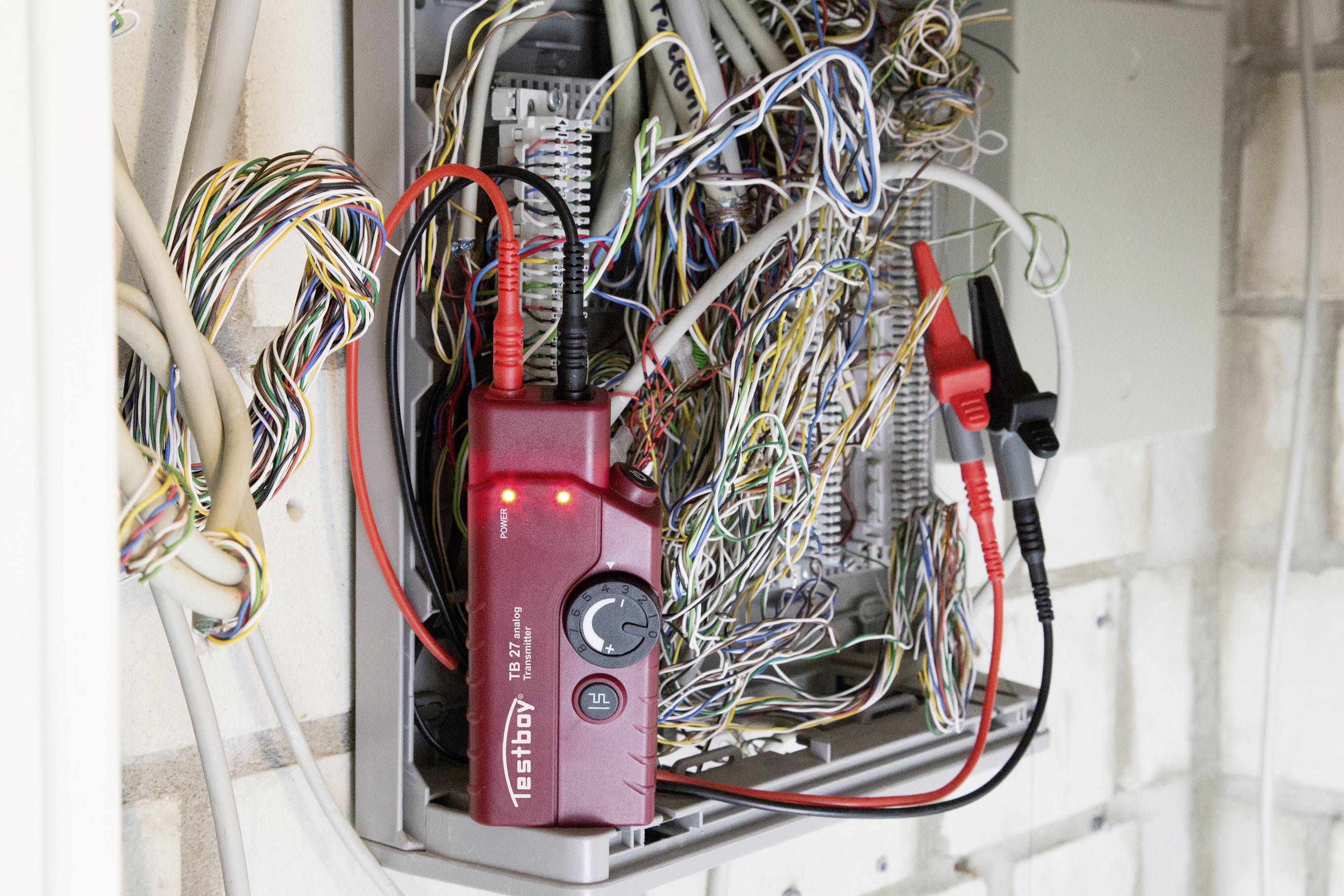 Ein rotes Diagnosegerät mit leuchtenden LEDs ist an ein komplexes Netzwerk von farbigen Kabeln in einem Verteilerkasten angeschlossen.