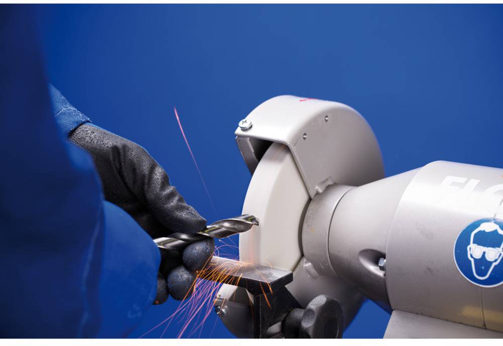 Eine Person schleift einen Metallbohrer an einer Tischschleifmaschine. Funken fliegen, während der Bohrer geschärft wird.