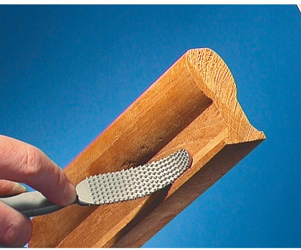 Eine Hand feilt mit einer Raspel eine Holzleiste. Die Textur und Form des Holzes sind deutlich zu erkennen.
