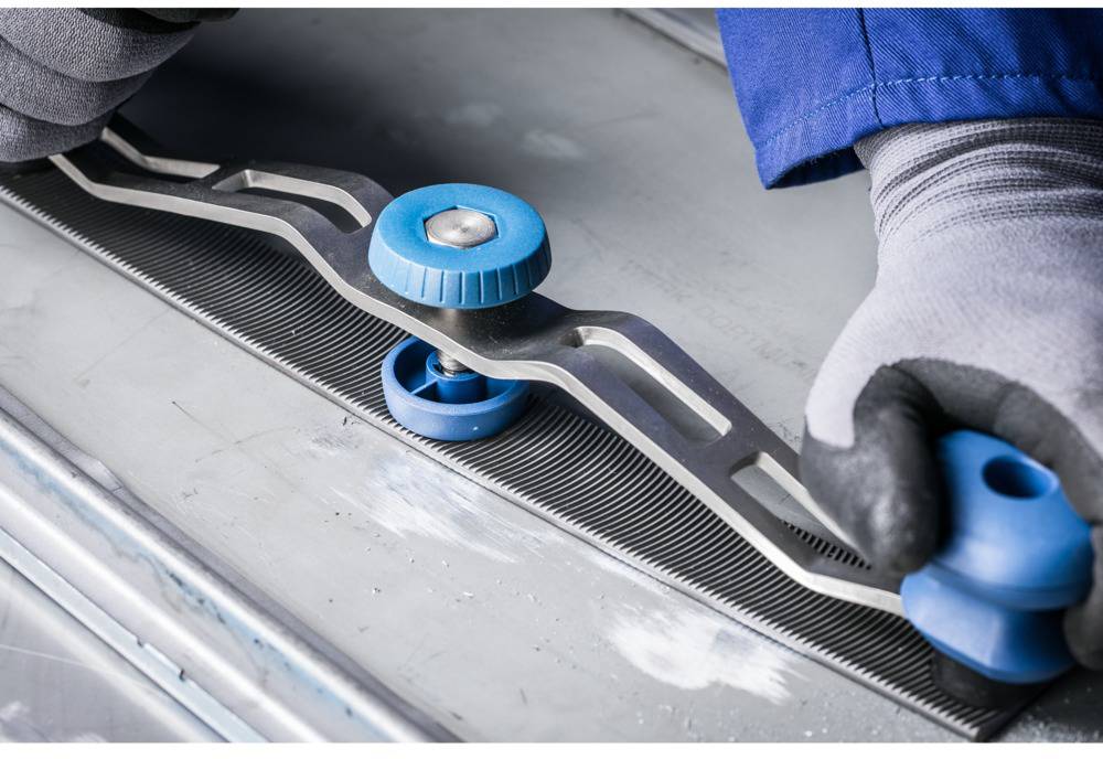 Eine Person justiert eine Säge mit einem blauen Spannwerkzeug. Das Bild zeigt eine Nahaufnahme der präzisen Handarbeit an der Maschine.