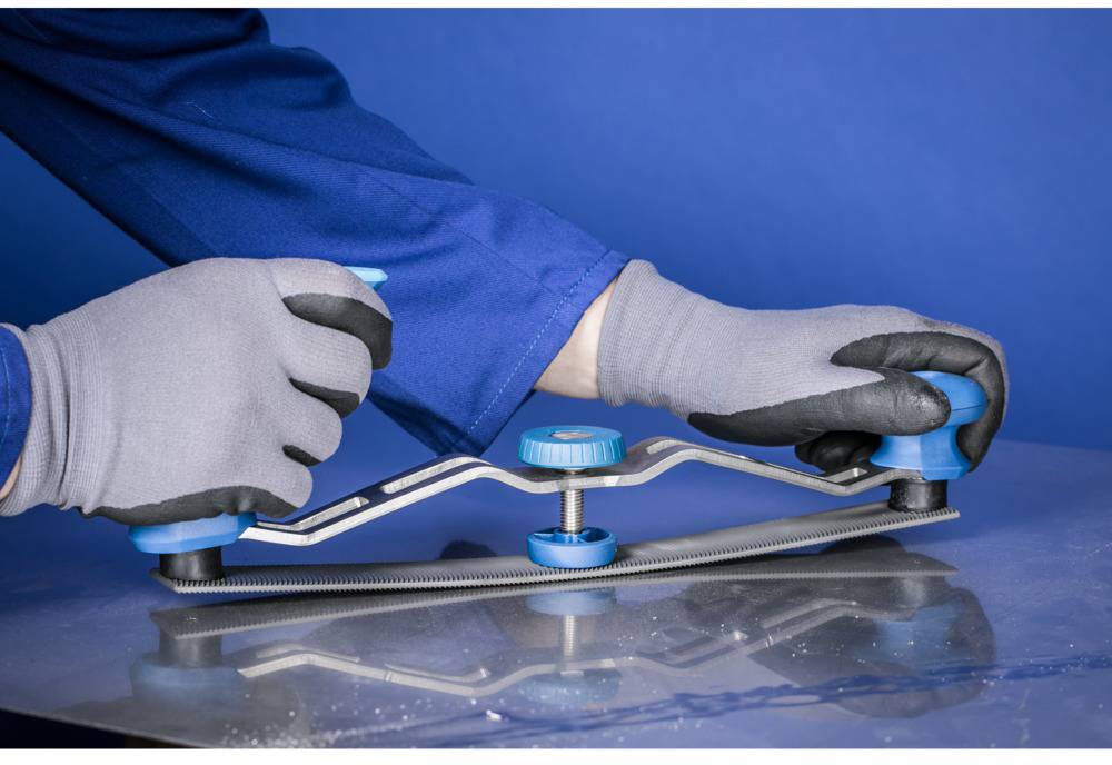 Eine Person in Arbeitskleidung und Handschuhen bewegt ein manuelles Werkzeug über ein Metallblech, um die Oberfläche zu glätten.