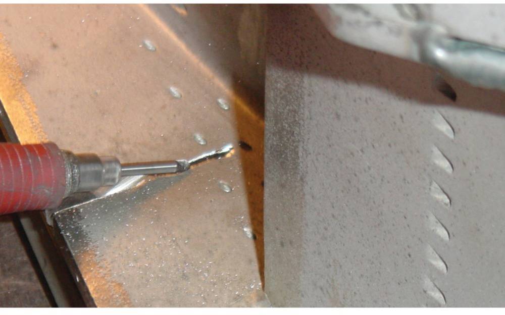 Nahaufnahme einer rotierenden Bohrmaschine, die ein Loch in eine Metallplatte bohrt. Metallspäne sind neben dem Bohrer sichtbar.