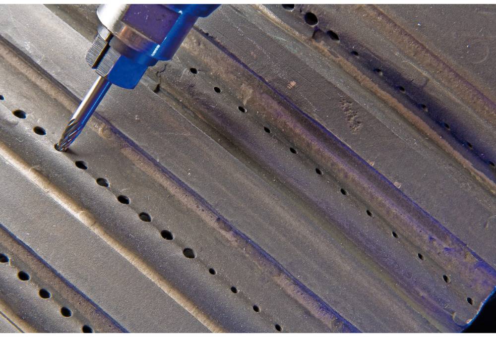 Nahaufnahme von einem Bohrer, der Löcher in ein gewelltes Metallblech bohrt. Die Bohrmaschine ist blau.