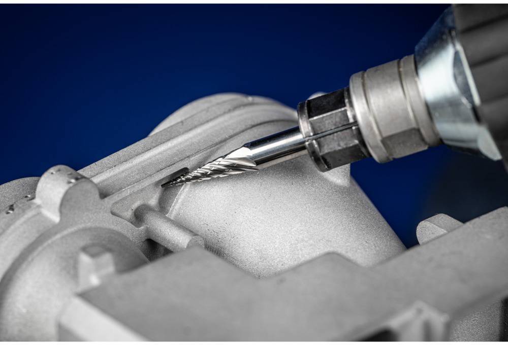 Nahaufnahme eines Bohrers, der eine Metalloberfläche präzise bearbeitet. Der Hintergrund ist blau und der Fokus liegt auf dem Bohrprozess.