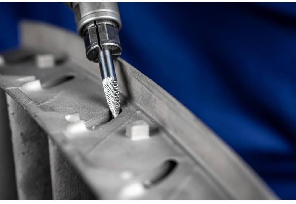 Nahaufnahme eines Bohrers, der Metalloberfläche bearbeitet. Der Hintergrund ist unscharf blau. Fokus liegt auf der Präzisionsarbeit.