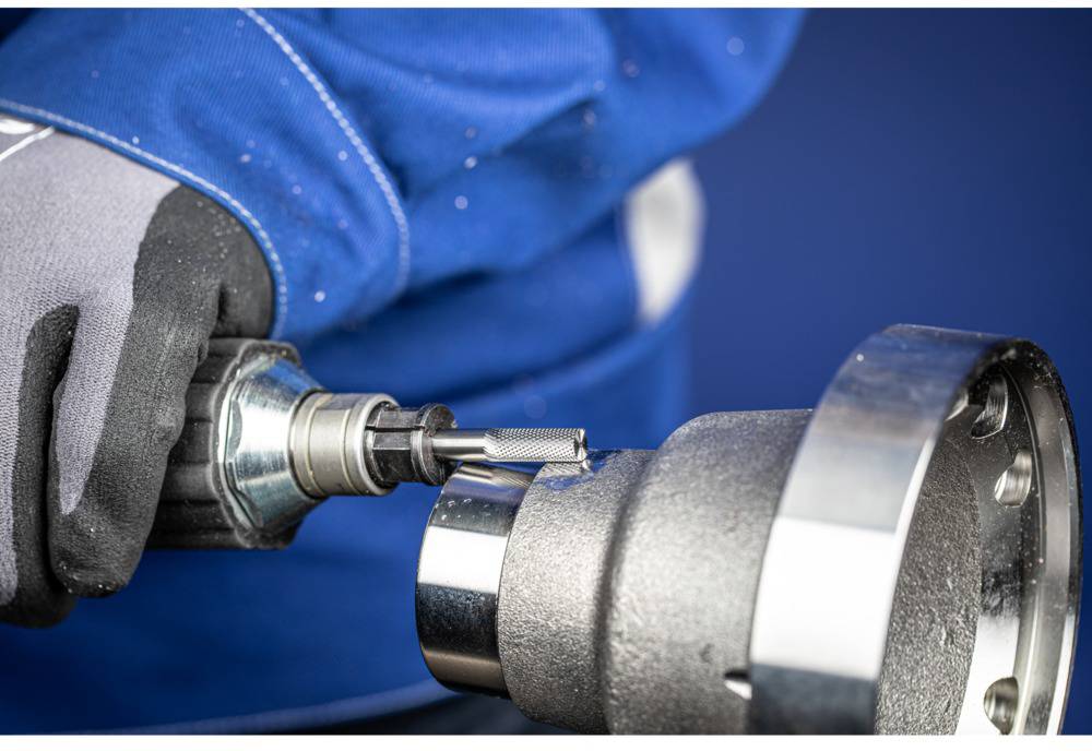 Arbeiter in blauer Jacke benutzt Werkzeug zur Bearbeitung eines Metallteils.