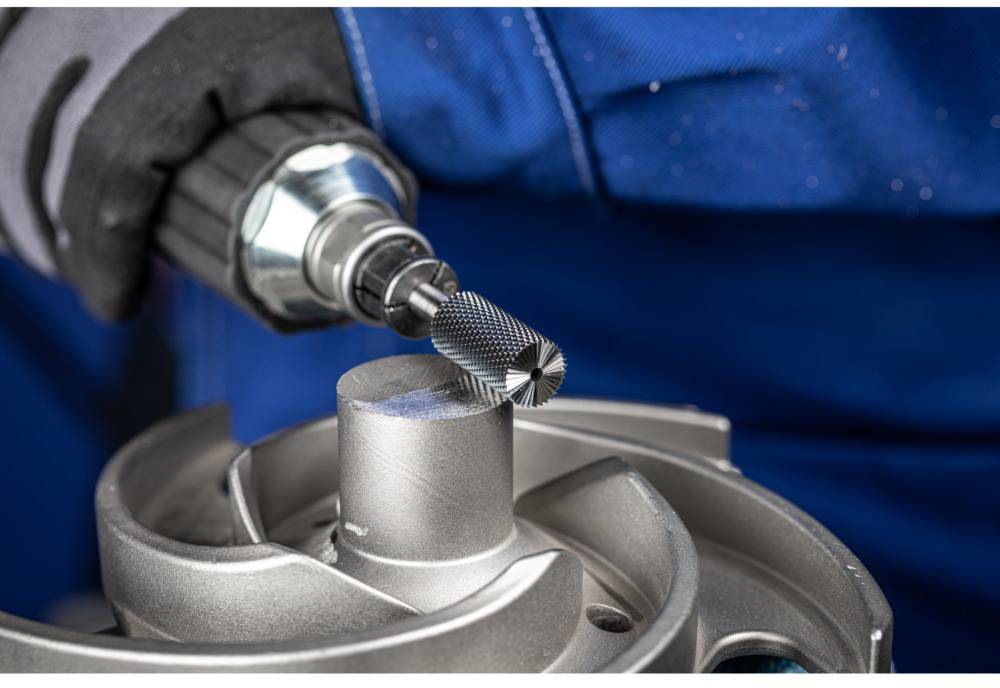 Eine Person bearbeitet ein Metallteil mit einem Schleifwerkzeug. Das Bild zeigt eine Nahaufnahme des Prozesses.