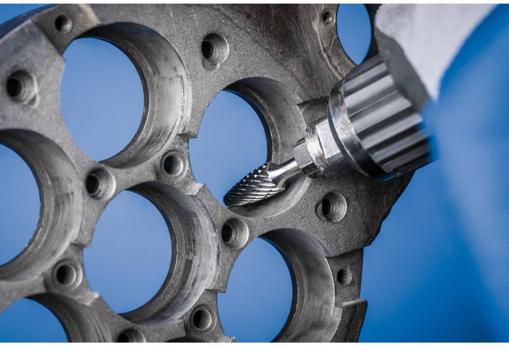 Fräsmaschine bearbeitet Metallteil mit mehreren runden Aussparungen. Das Bild zeigt eine Detailaufnahme des Fertigungsprozesses.