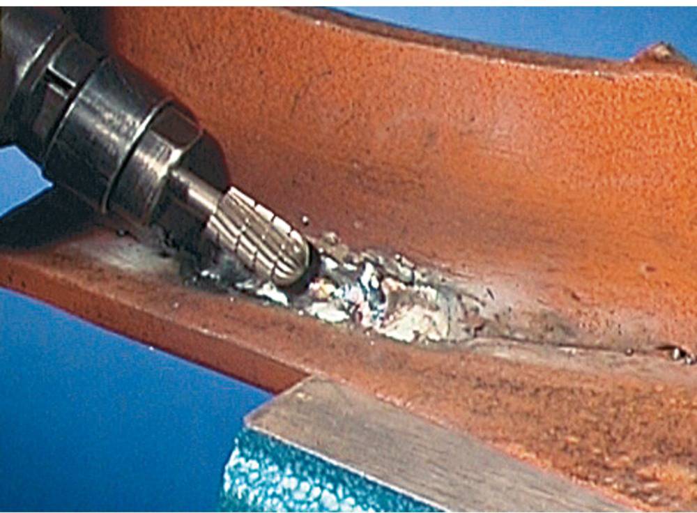 Ein rot lackiertes Metallstück wird mit einem rotierenden Werkzeug bearbeitet, um die Schweißnaht zu glätten.