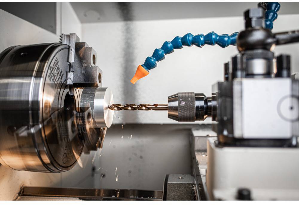 Ein Drehmaschinenarbeitsplatz, der Metall bearbeitet, zeigt einen rotierenden Metallblock und einen Bohrer, der das Material durchdringt.