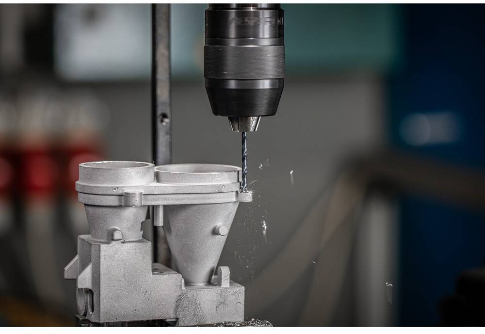 Eine Maschine bohrt präzise Löcher in ein Metallteil in einer Werkstattumgebung, Fokus auf den Bohrer und das bearbeitete Werkstück.