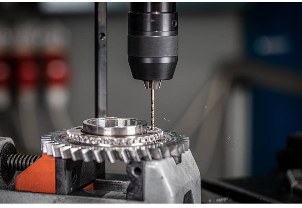 Nahaufnahme eines Bohrers, der ein Metallrad mit Zahnrädern in einer Werkstatt bearbeitet.