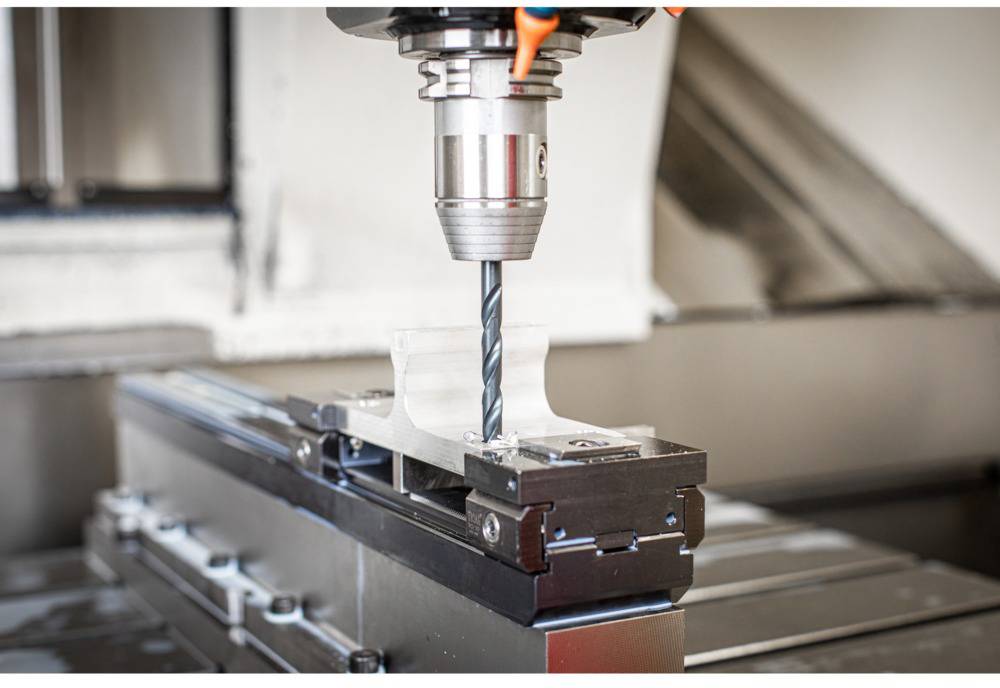 Nahaufnahme einer CNC-Fräsmaschine, die ein Werkstück bearbeitet. Das Bild zeigt den Fräskopf und die Halterung des Werkstücks.