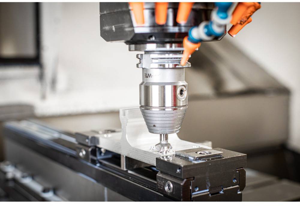 Fräsmaschine bearbeitet Metallstück, während Kühlmittel durch orangefarbene Schläuche aufgetragen wird. Fokus auf Präzisionsarbeit.
