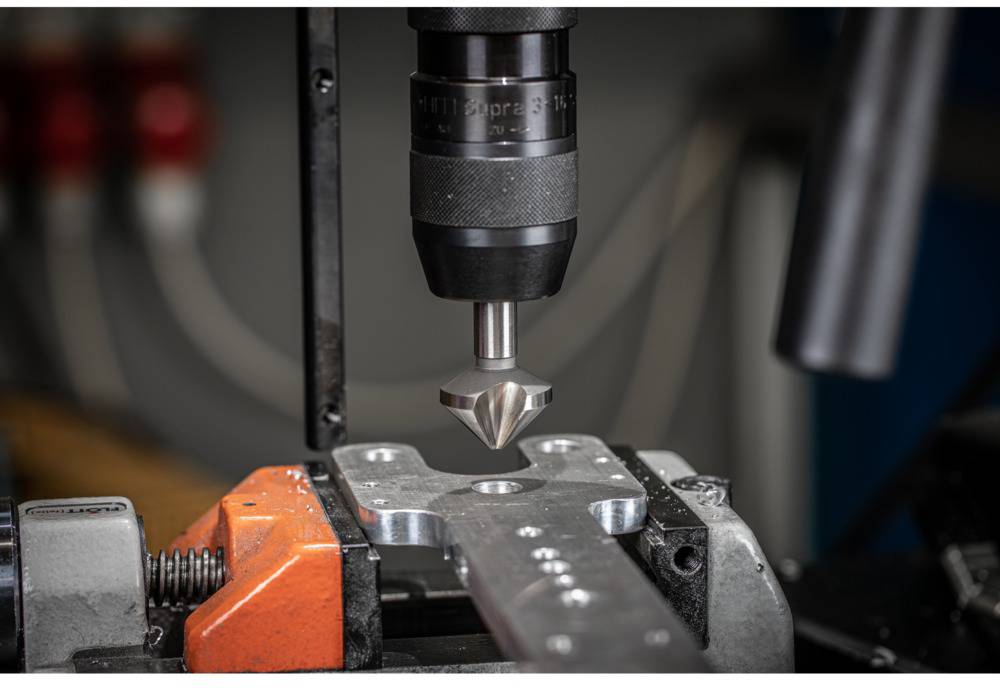 Nahaufnahme einer CNC-Maschine, die Metall bearbeitet; ein Bohrer senkt präzise in ein Werkstück ein. Industrieumgebung im Hintergrund.