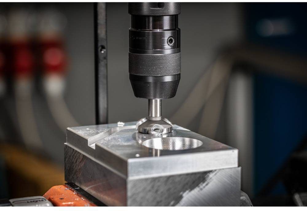 Eine Werkzeugmaschine fräst präzise ein kreisförmiges Muster in einen Metallblock, umgeben von industrieller Ausrüstung.