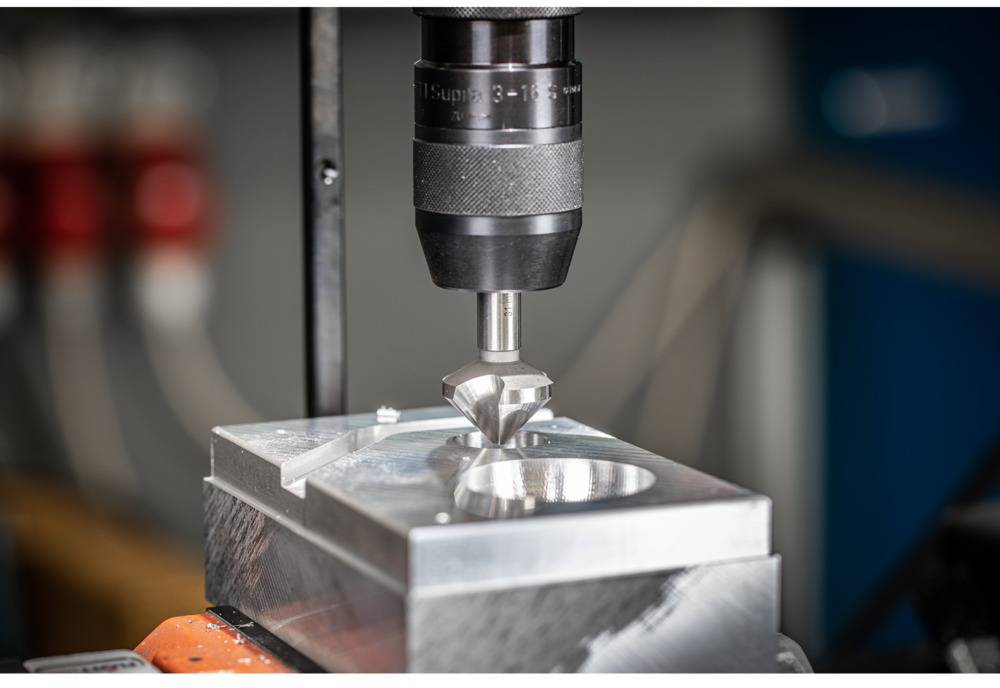 Eine CNC-Fräsmaschine bearbeitet präzise ein Metallblock-Werkstück mit einem rotierenden Werkzeug in einer Werkstattumgebung.