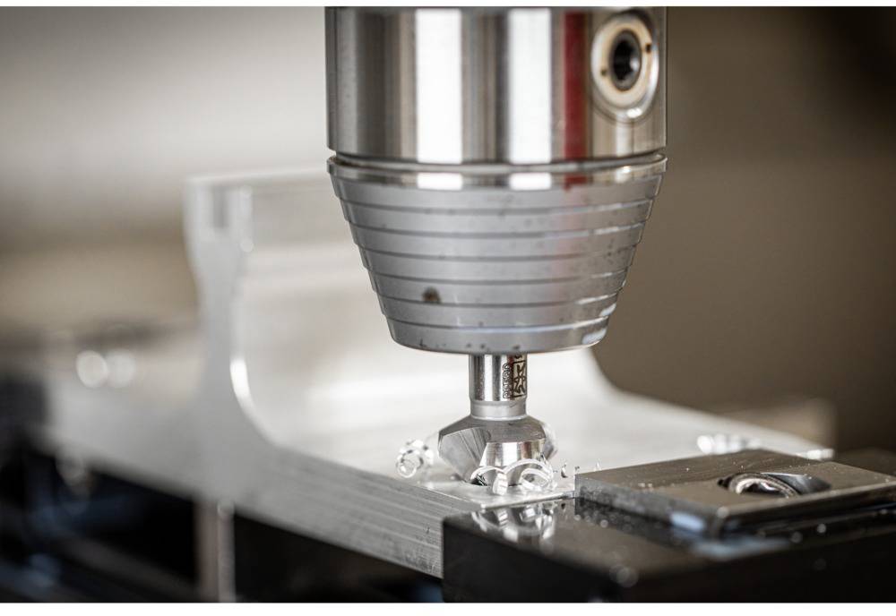 Eine CNC-Fräsmaschine bearbeitet präzise ein Metallstück. Der Fokus liegt auf dem Fräskopf, der Späne vom Werkstück entfernt.