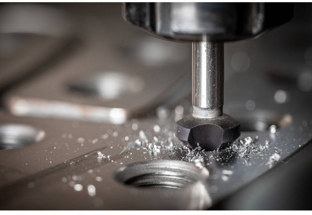 Nahaufnahme einer CNC-Fräsmaschine, die Metall bearbeitet. Metallspäne sind zu sehen, während die Fräse Löcher auf einer Metallplatte formt.