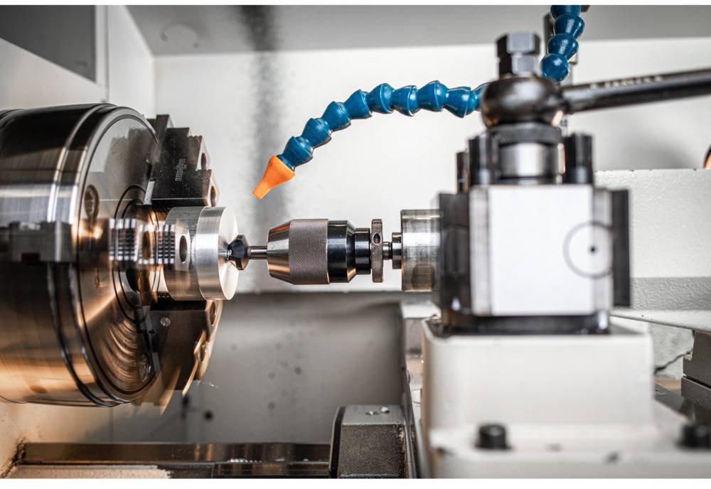 Eine CNC-Drehmaschine bearbeitet ein Metallstück. Der Bohrer präzisiert die Oberfläche, während ein Kühlmittelschlauch die Hitze reduziert.