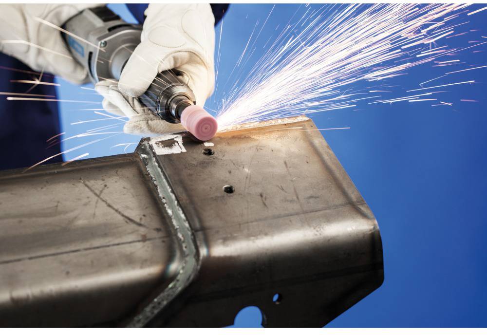Arbeiter schleift Metall mit einem Gerät, Funken fliegen. Nahaufnahme auf blauen Hintergrund.