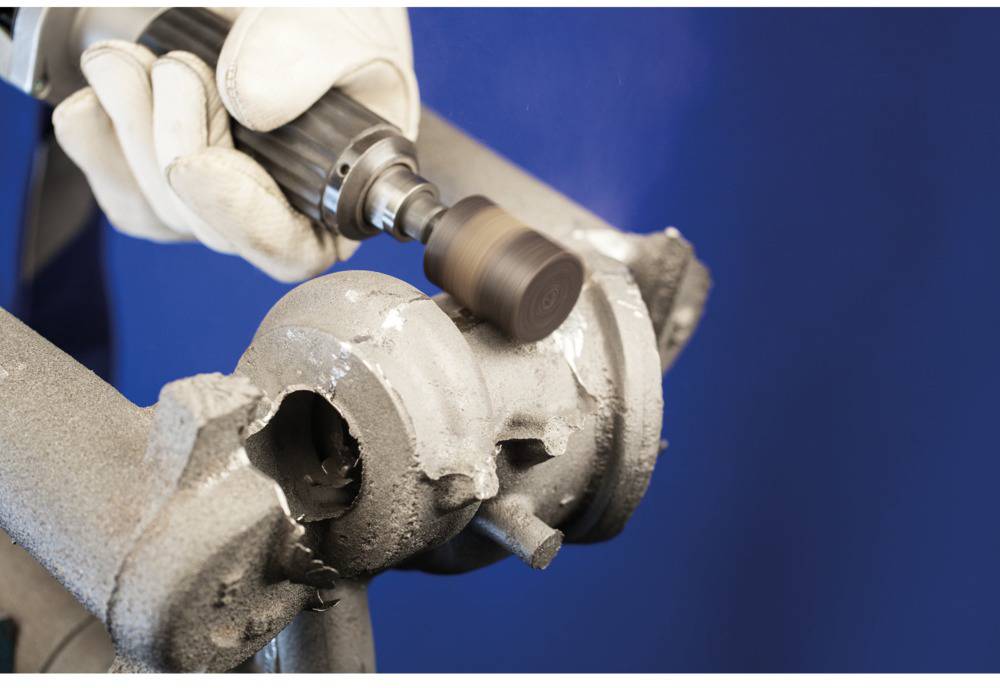 Eine Person verwendet ein elektrisches Schleifwerkzeug, um eine Metalloberfläche zu glätten. Schutz-Handschuhe sind sichtbar.