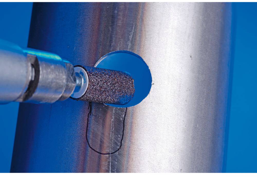 Ein Metallrohr wird mit einem rotierenden Schleifaufsatz bearbeitet, das eine runde Öffnung glättet. Hintergrund in Blau.
