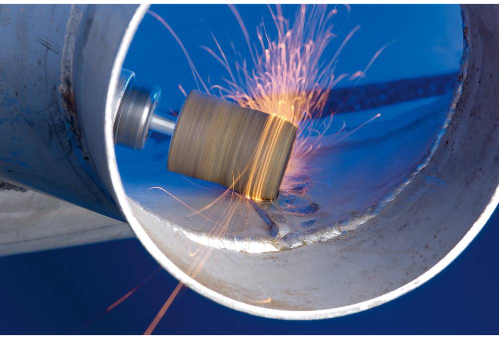 Ein Schleifwerkzeug bearbeitet das Innere eines Metallrohrs. Funken fliegen von der Kontaktstelle.