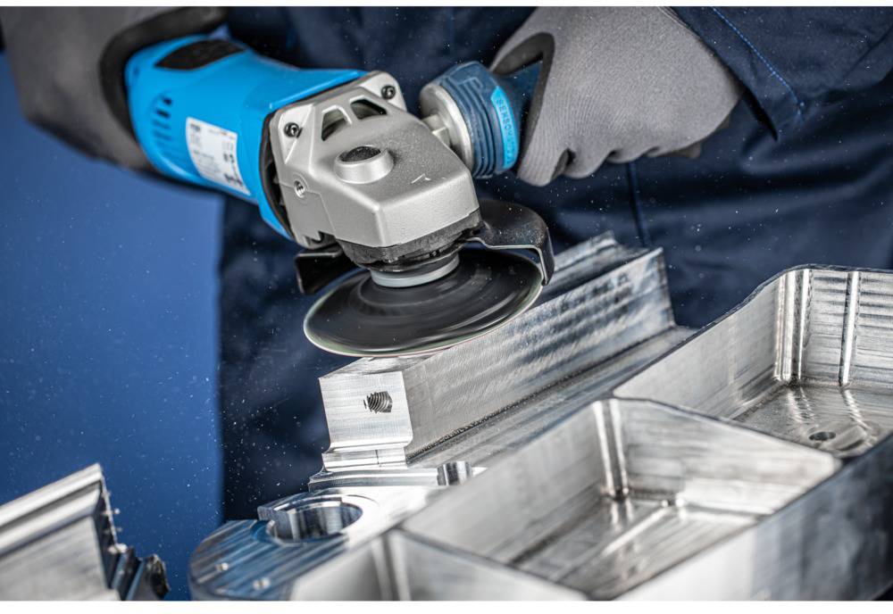 Person mit Handschuhen benutzt einen Schleifer, um Metall zu bearbeiten. Späne fliegen, Detailarbeit an einer Maschine.
