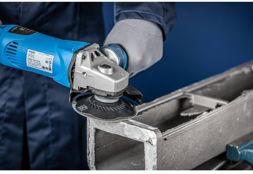 Eine Person schleift mit einem blauen Winkelschleifer eine Metallkante. Im Hintergrund sind unscharfe Werkzeuge erkennbar.