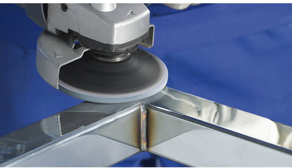 Eine Schleifmaschine bearbeitet eine Kante eines Metallrahmens, während er gewinkelt liegt. Das Werkzeug entfernt Material für eine glatte Oberfläche.