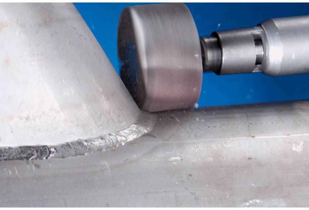 Nahaufnahme eines Metallbearbeitungsprozesses: Eine Maschine schleift die Kante eines Metallstücks glatt.