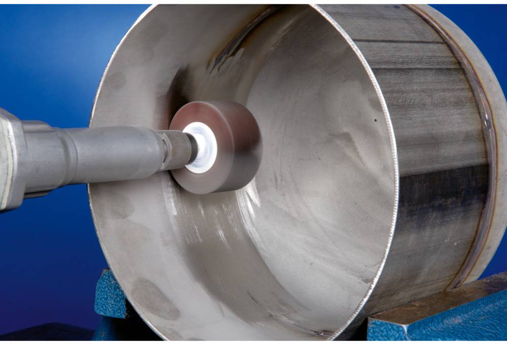 Das Bild zeigt ein Schwerlastschleifwerkzeug, das die Innenseite eines Metallrohrs bearbeitet. Der Hintergrund ist blau.