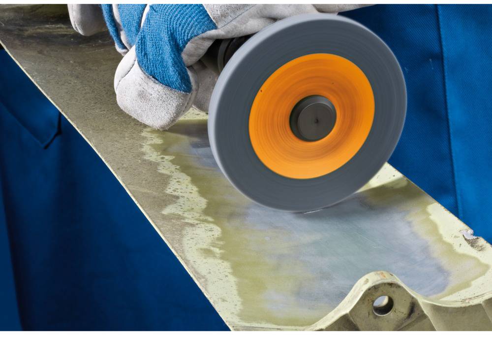 Ein Arbeiter schleift eine Metalloberfläche mit einem rotierenden Werkzeug. Handschuhe und Schutzkleidung sind sichtbar.