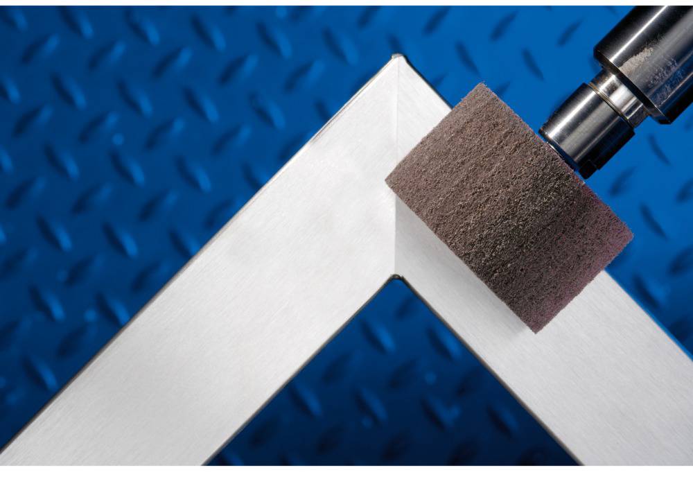 Schleifmaschine poliert eine rechtwinklige Metallkante auf einem blauen Hintergrund.