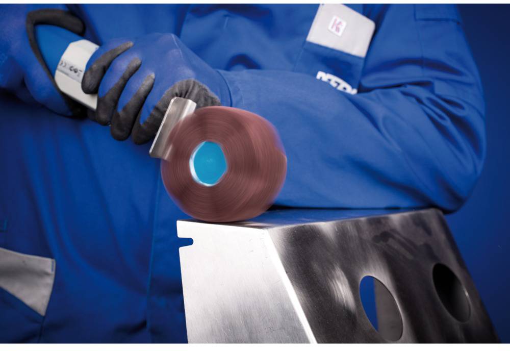 Person in blauer Arbeitskleidung schleift eine Metalloberfläche mit einer rotierenden Polierscheibe.