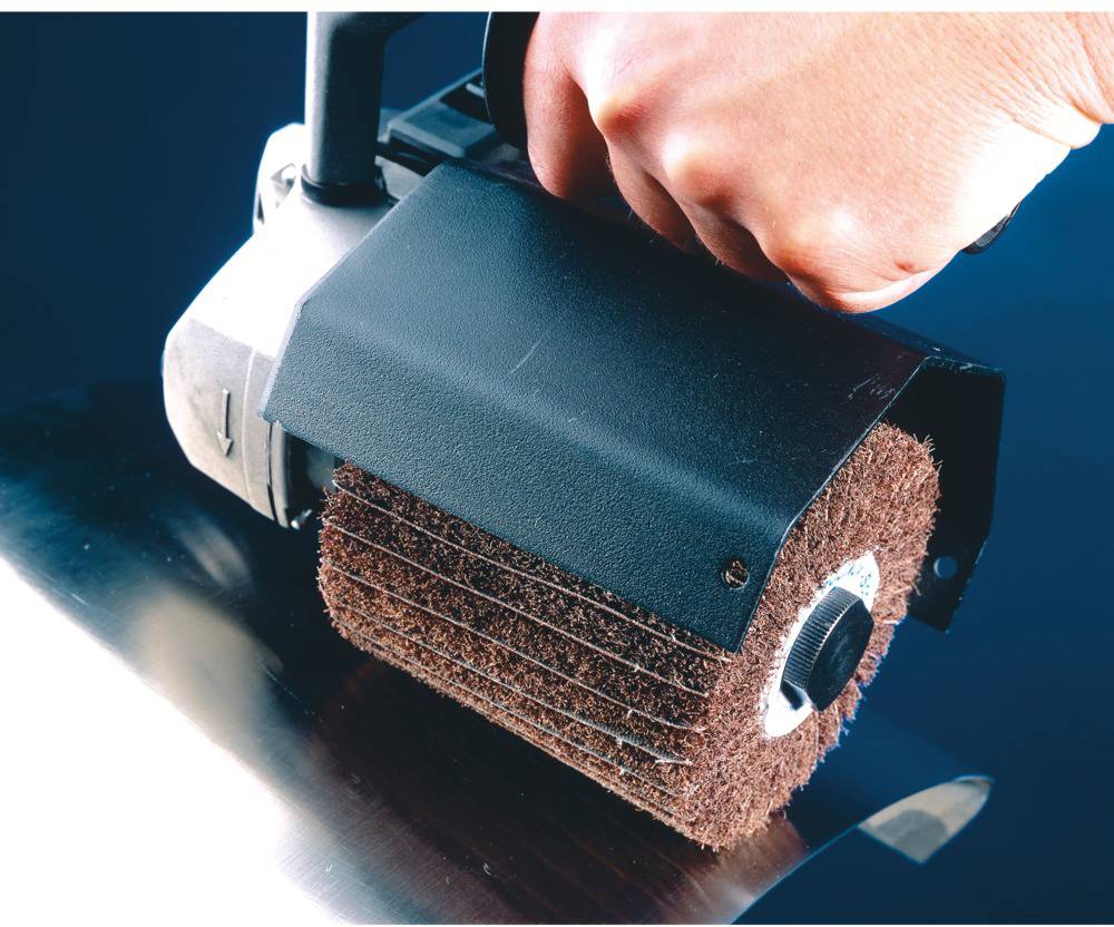 Eine Hand hält ein elektrisches Schleifgerät mit einer rotierenden Walze, das auf einer Metalloberfläche verwendet wird.