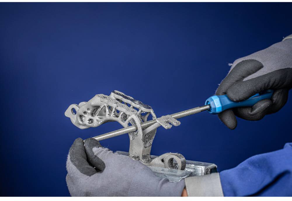 Eine Person in Handschuhen bearbeitet ein Metallteil mit einer Feile. Der Hintergrund ist dunkelblau.