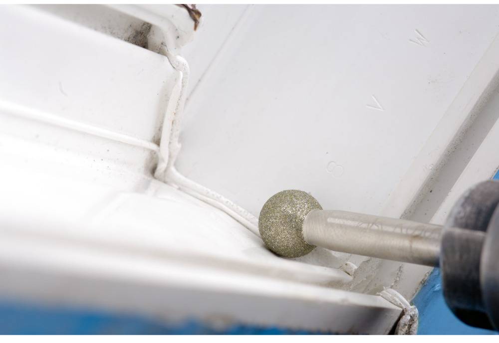 Ein Schleifwerkzeug glättet die Kanten einer weißen Fliese an einer Wand. Das Werkzeug hat eine Metallkugel am Ende.