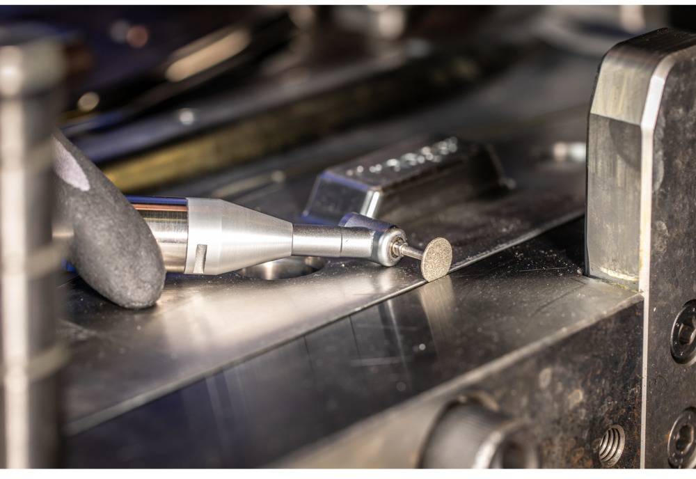 Nahaufnahme eines Winkelschleifers auf einer metallischen Oberfläche, mit einer kleinen Schleifscheibe an der Spitze.